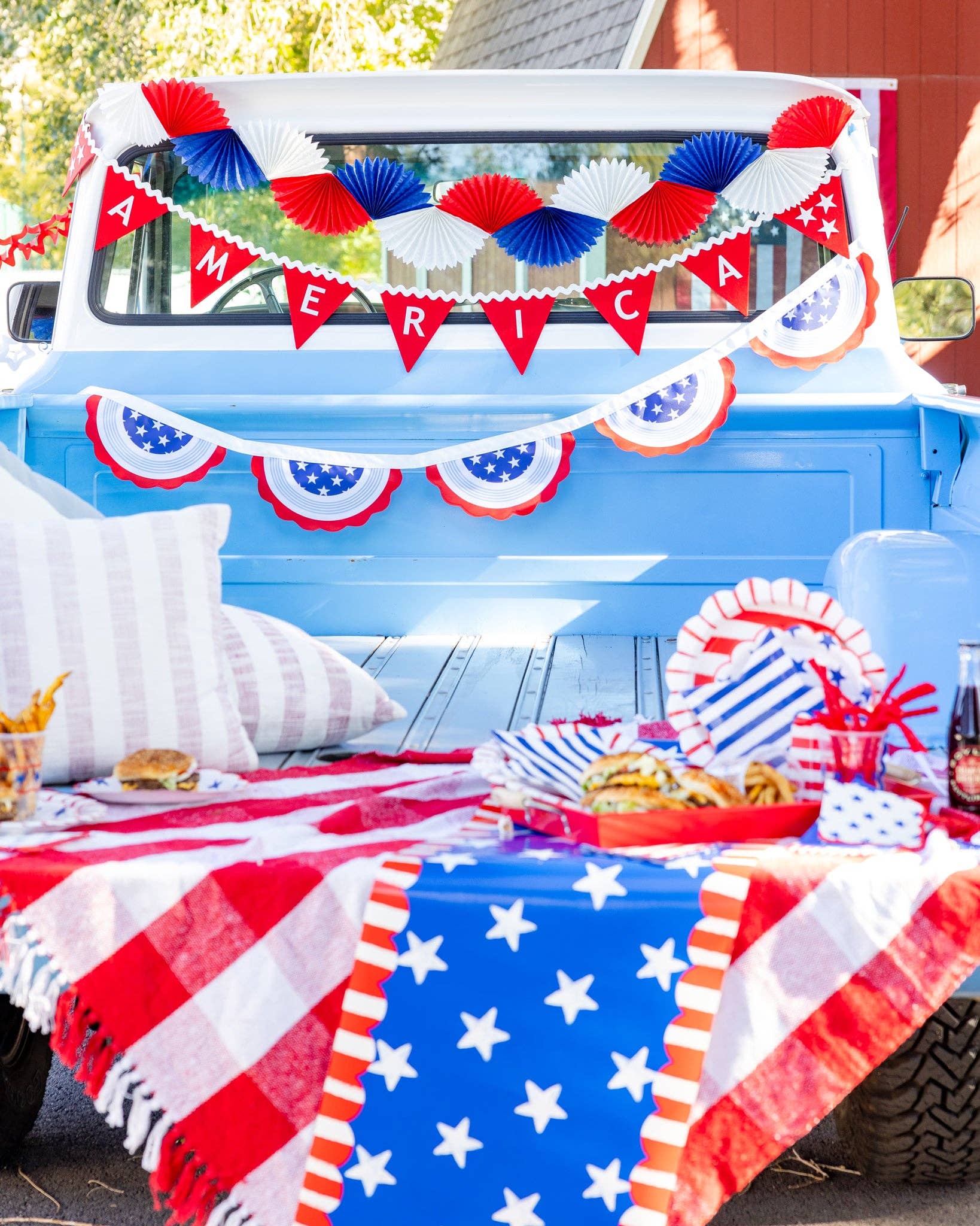 Close-up of vintage truck bed styled as a 4th of July picnic with America felt pennant banner, paper fan garland, bunting, and summer food