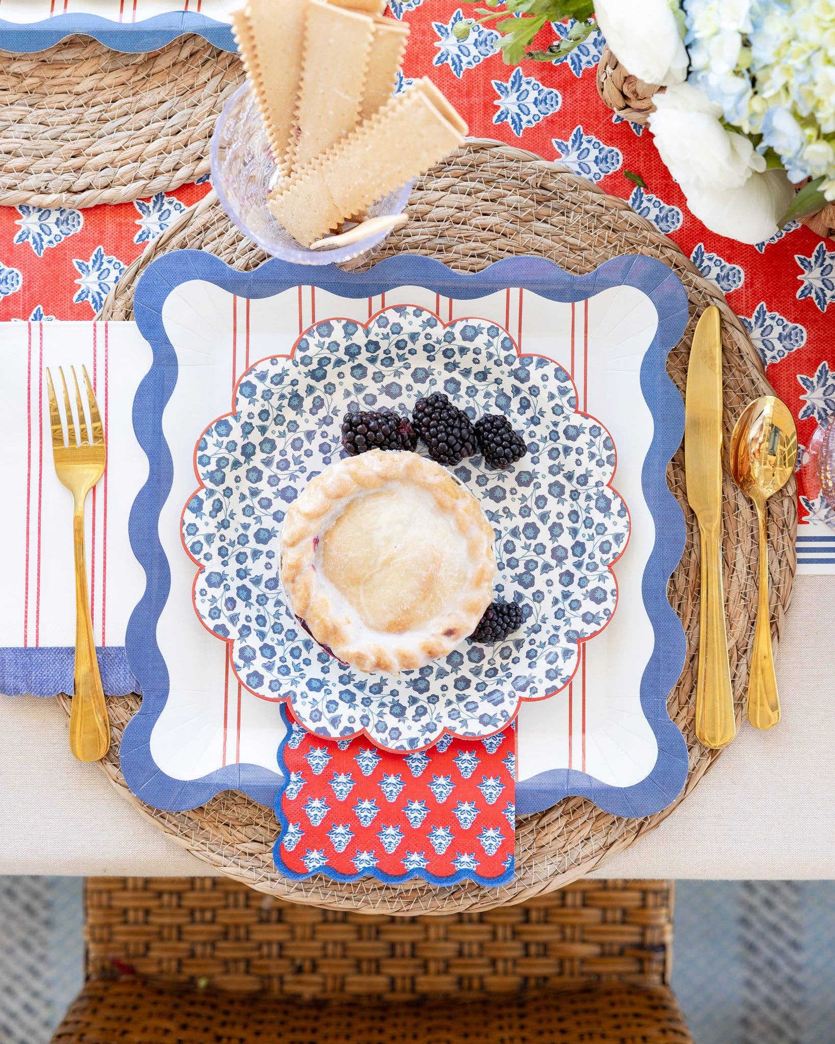 Overhead place setting with blue wave dinner plate, ditsy floral dessert plate, and red block print cocktail napkin on Americana tablescape