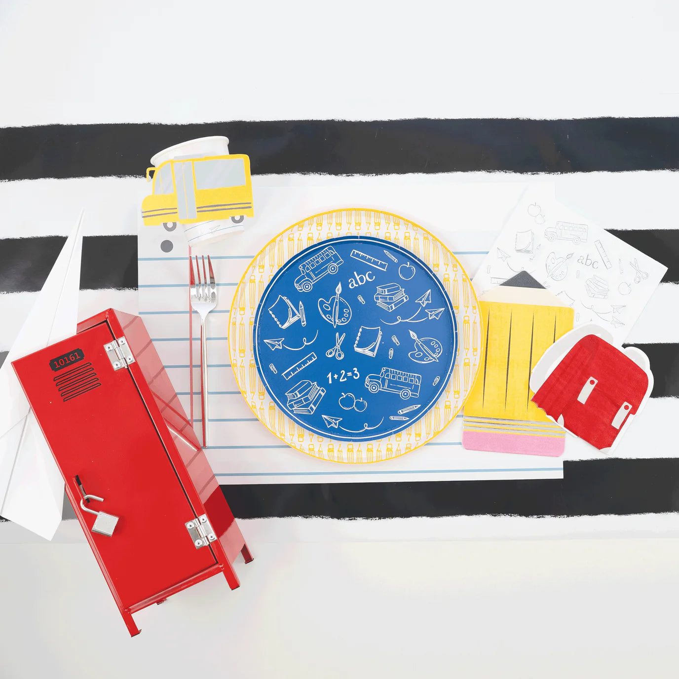 Blue notebook‑theme place setting showing yellow pencil dinner plate under blue icon salad plate.