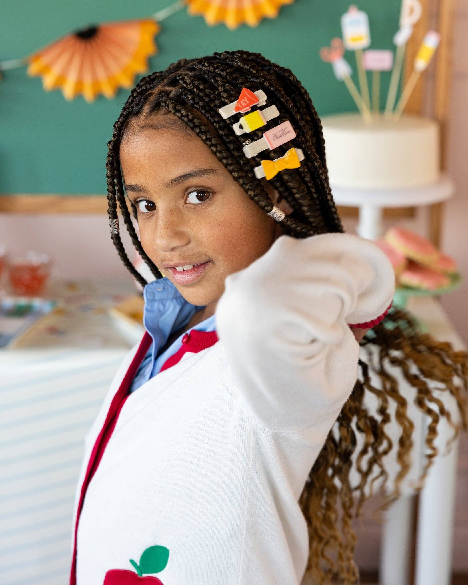 Close-up of young girl with braids wearing four back to school hair clips including YAY megaphone, pencil, pink eraser, and ruler bow