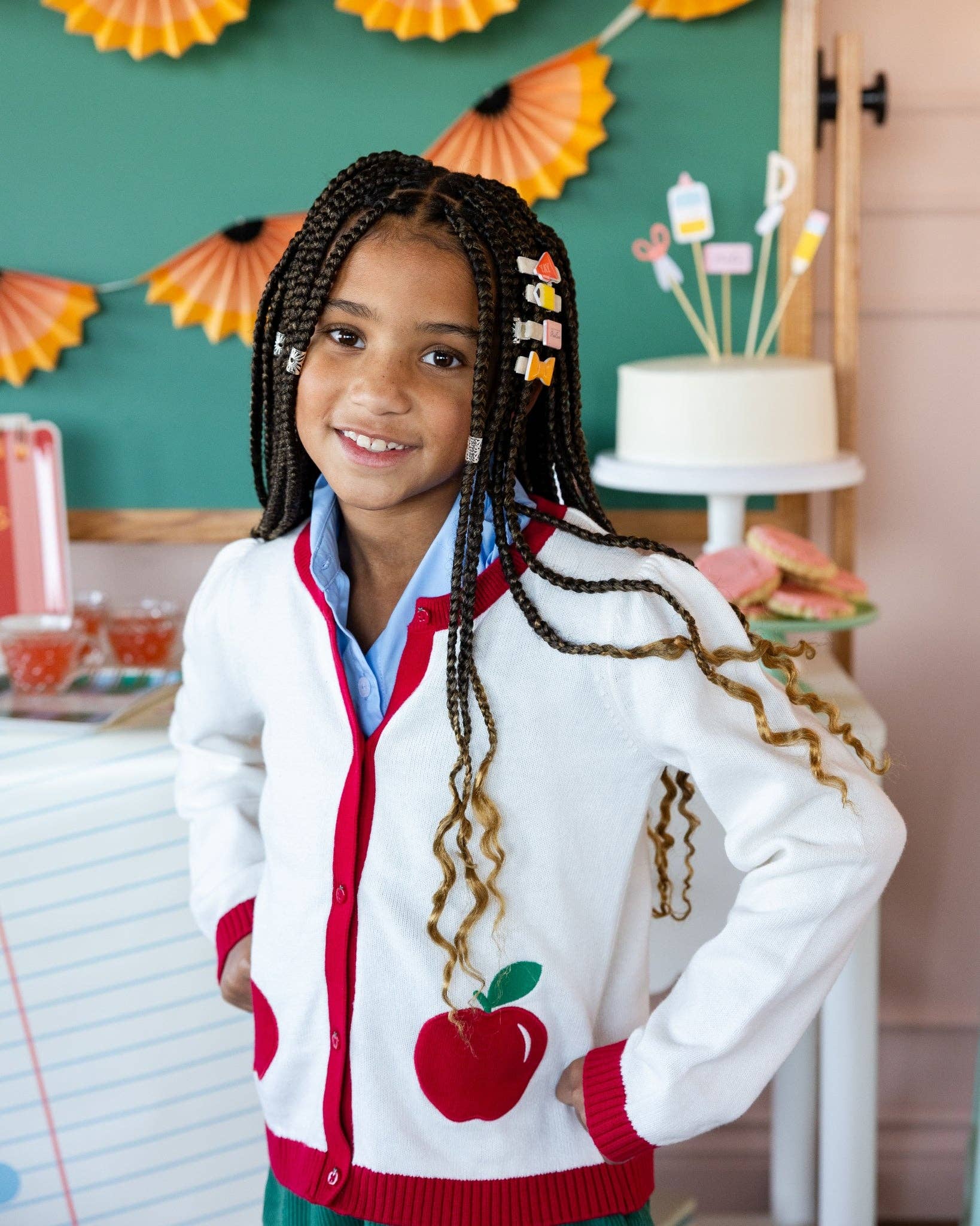 Young girl with long braided hair wearing back to school hair barrettes at styled classroom party with pencil shaving banner and chalkboard backdrop