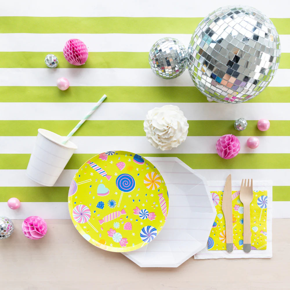Lime-green striped table with disco balls and “It’s a Birthday” candy plate at center, surrounded by party cutlery and pastel decorations.