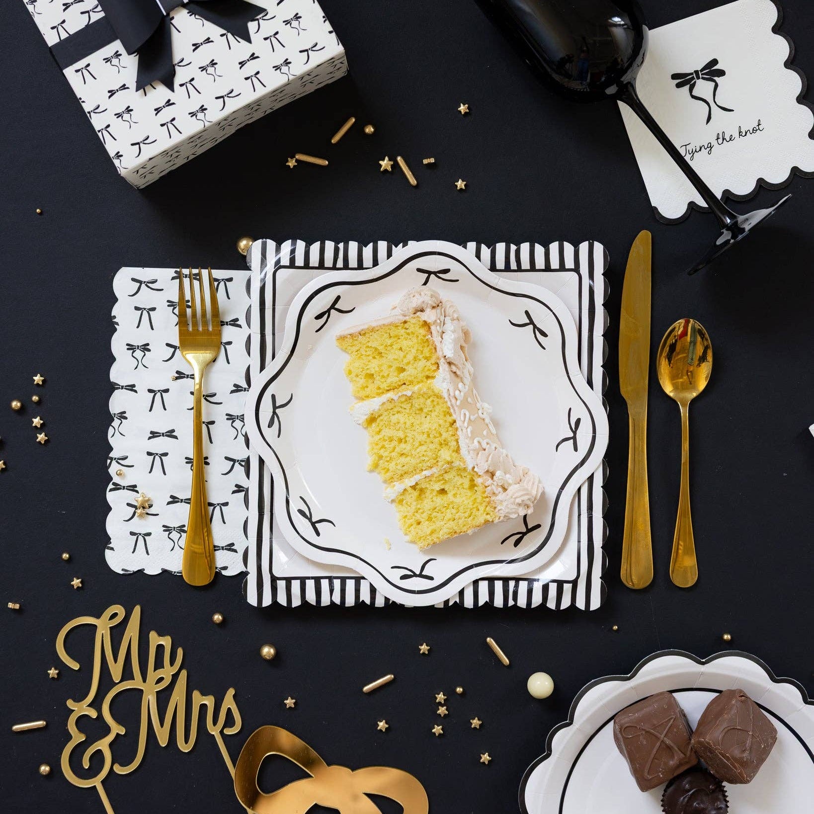 Black bow scalloped dessert plate displayed on black bachelorette table setting with cake slice and gold cutlery