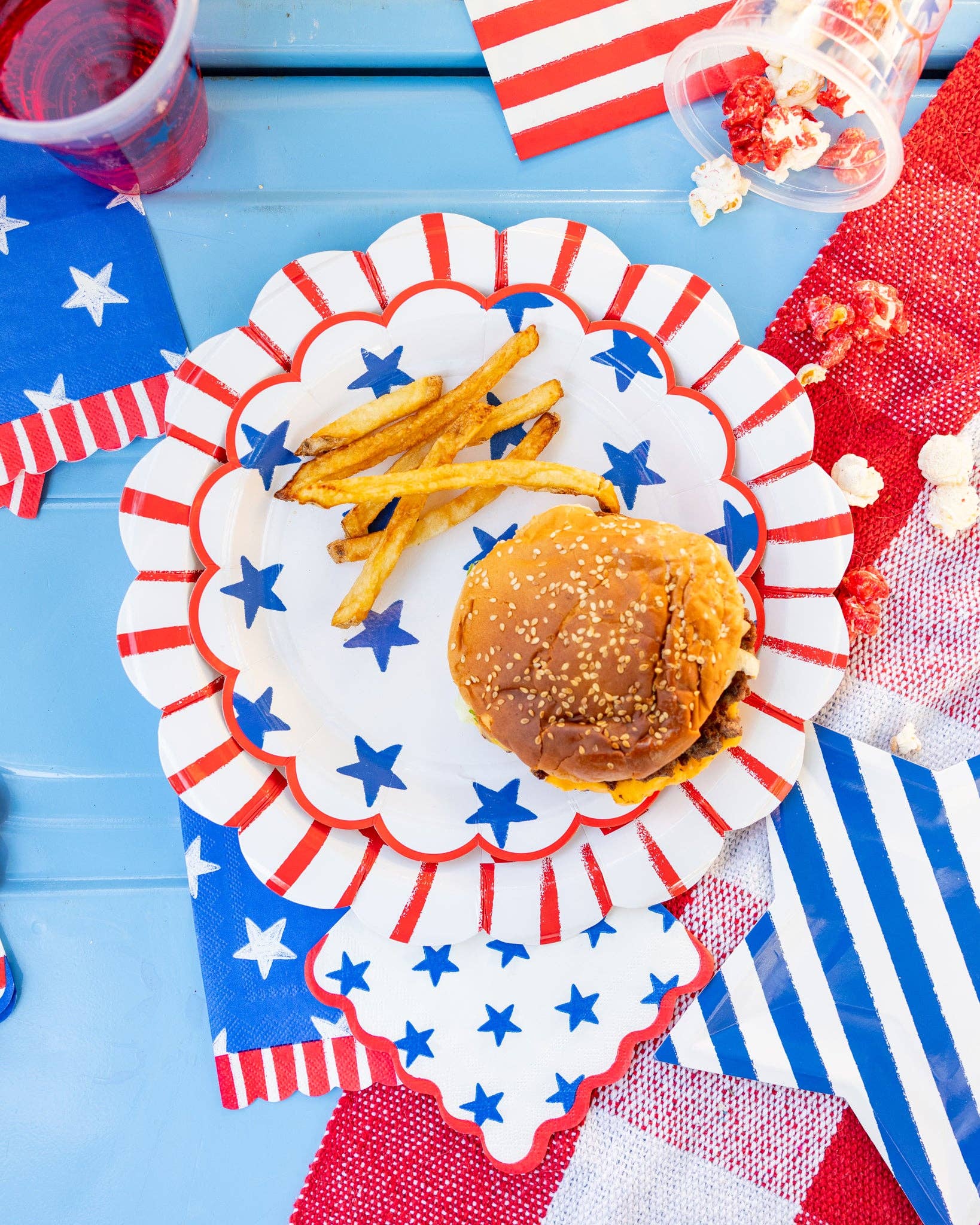 Overhead view of blue star scalloped plate nested inside red striped scalloped dinner plate with a burger and fries on a patriotic tablescape