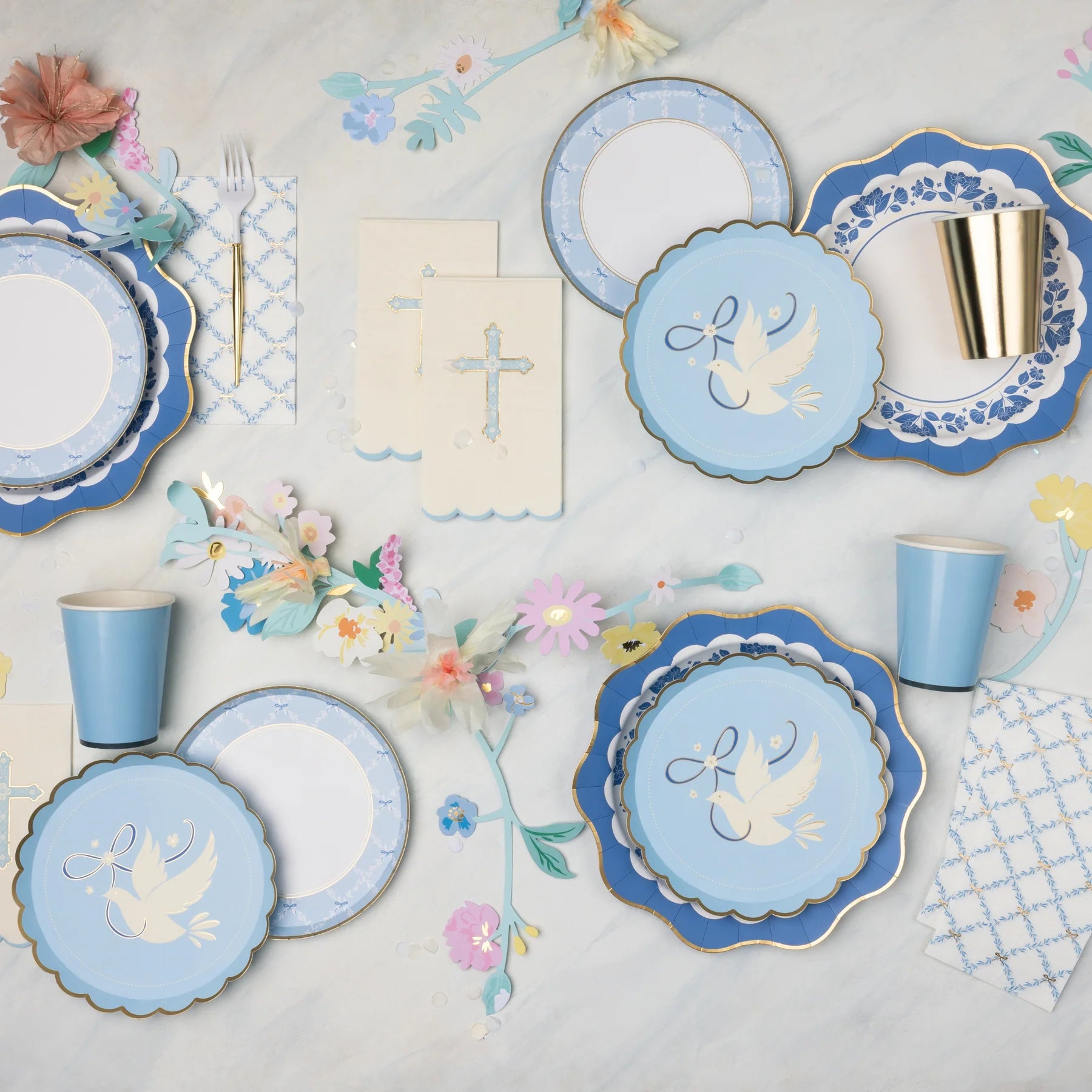 Blue trellis bow scalloped paper plates layered with navy dove plates and floral print plates on a baptism tablescape with cross napkins, gold paper cups, and pastel paper flower garland.