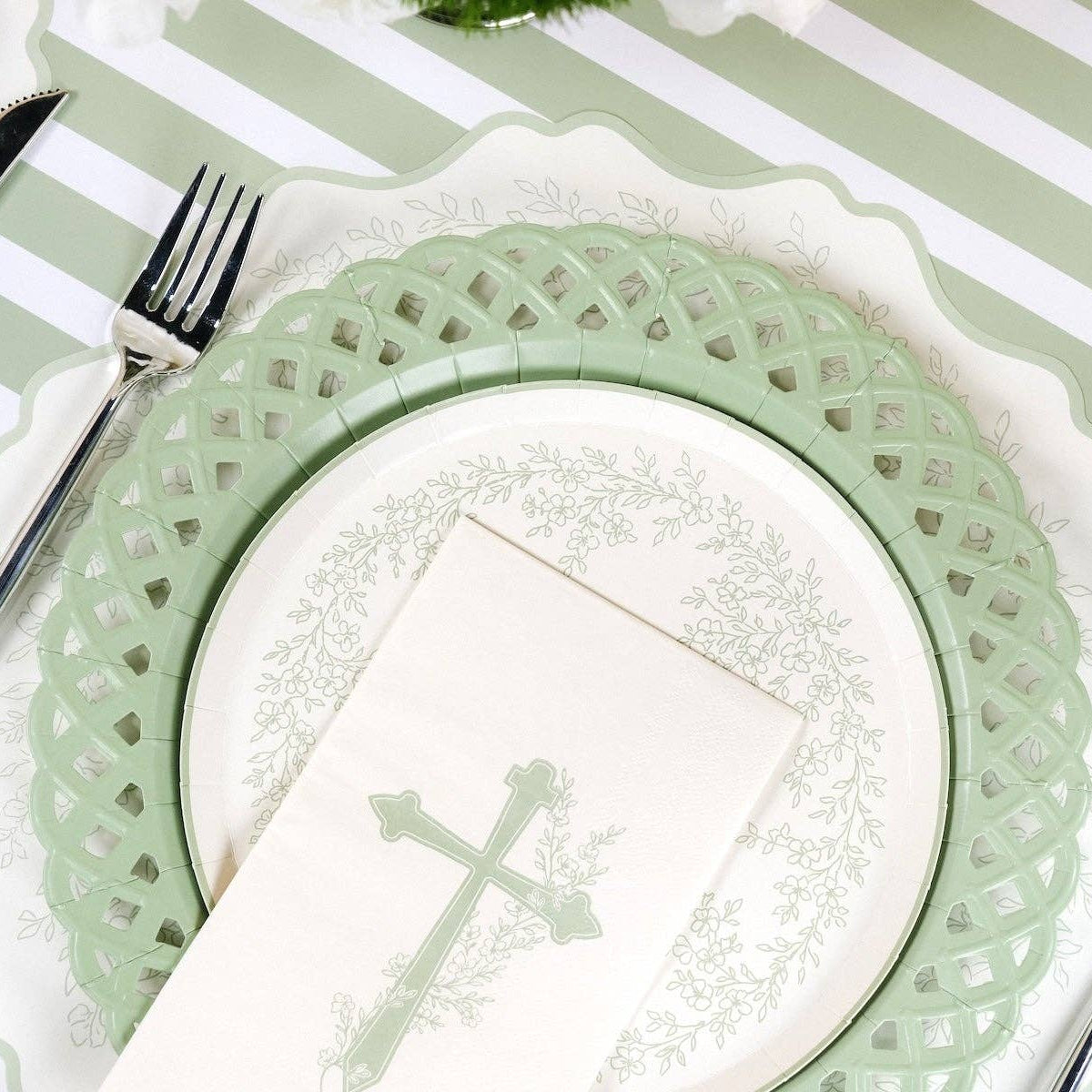 An angled close up of a botanical cross guest towel resting on an elegant floral and lattice paper plate.
