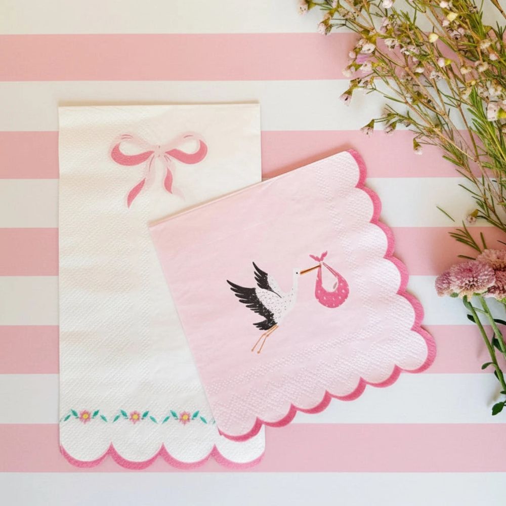 Pink bow napkin next to a stork baby shower napkin on striped background