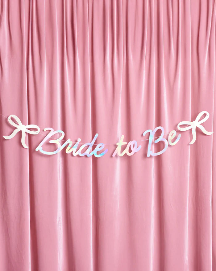 Full Bride to Be iridescent foil banner with bow accents hung on pink velvet backdrop