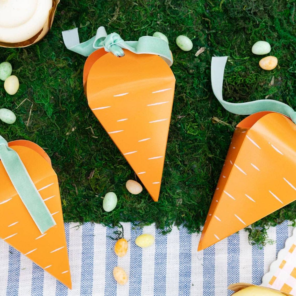 Three carrot treat boxes styled on moss with pastel candy eggs for Easter display