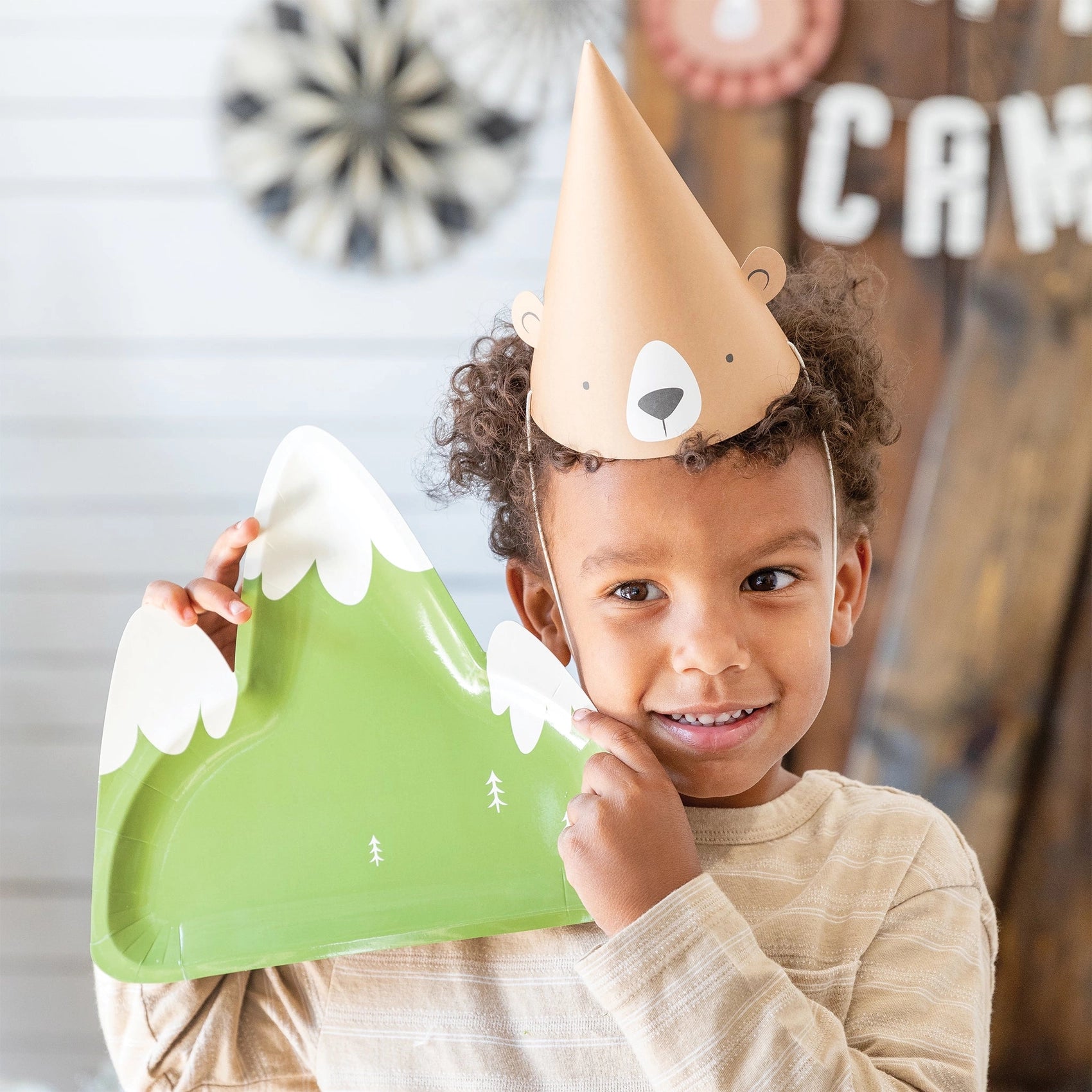 A smiling child wearing a bear party hat and holding the mountain plate up to the camera with joy.