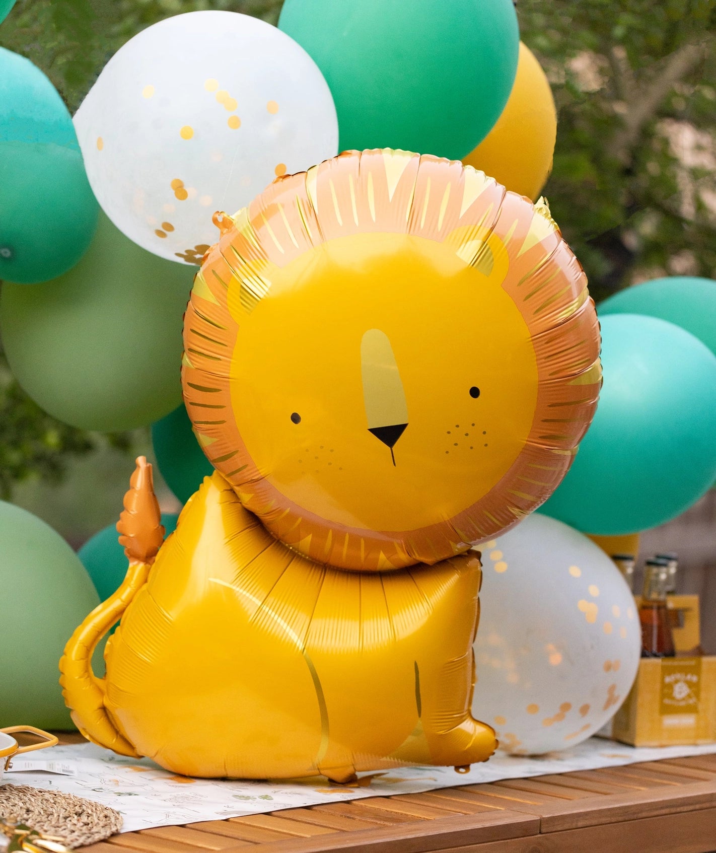 Yellow lion-shaped Mylar balloon against a backdrop of green and white balloons for a safari-themed party.