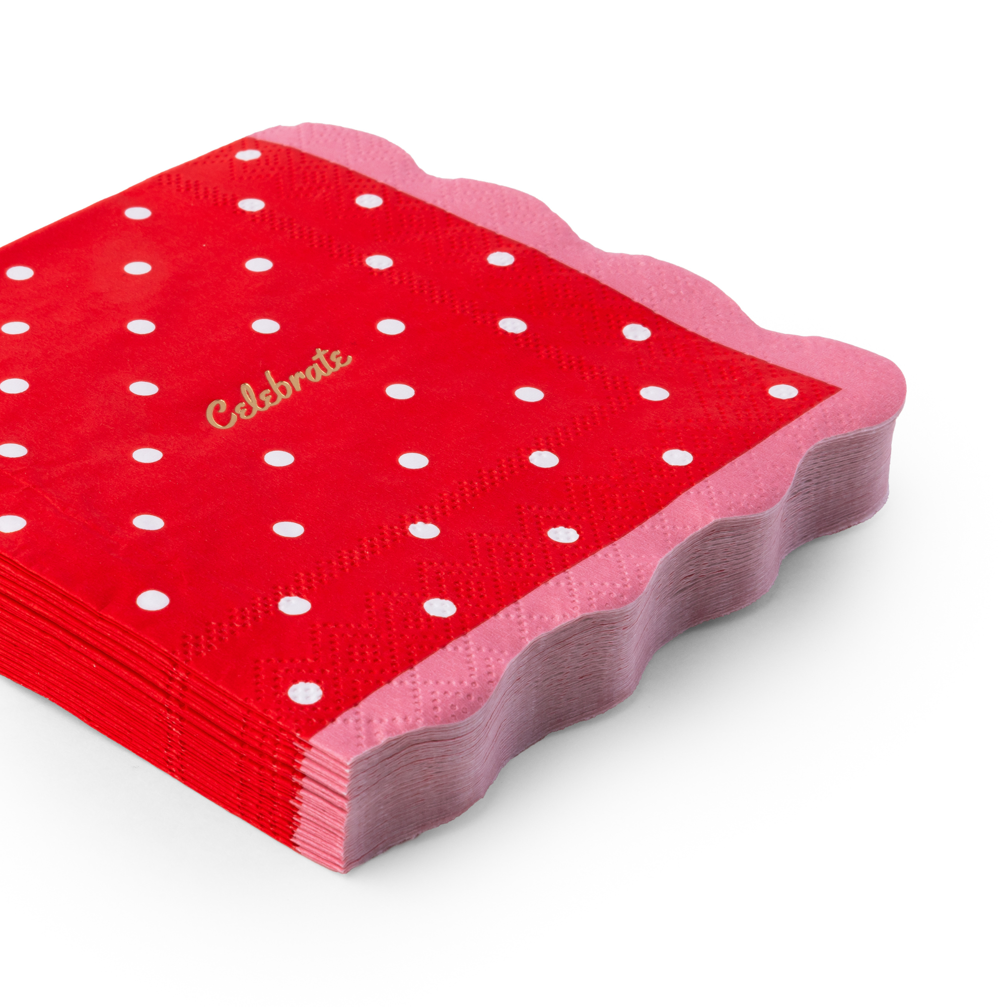 Angled view of stacked red polka dot celebrate cocktail napkins showing gold foil script, pink scalloped edge, and 3-ply thickness