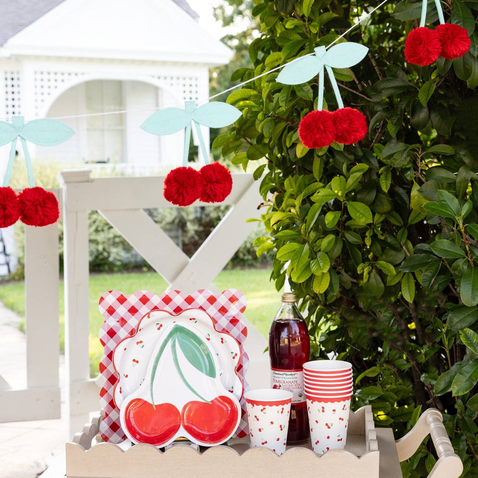 Cherry banner hanging outdoors above a party table with cherry themed plates and cups.

