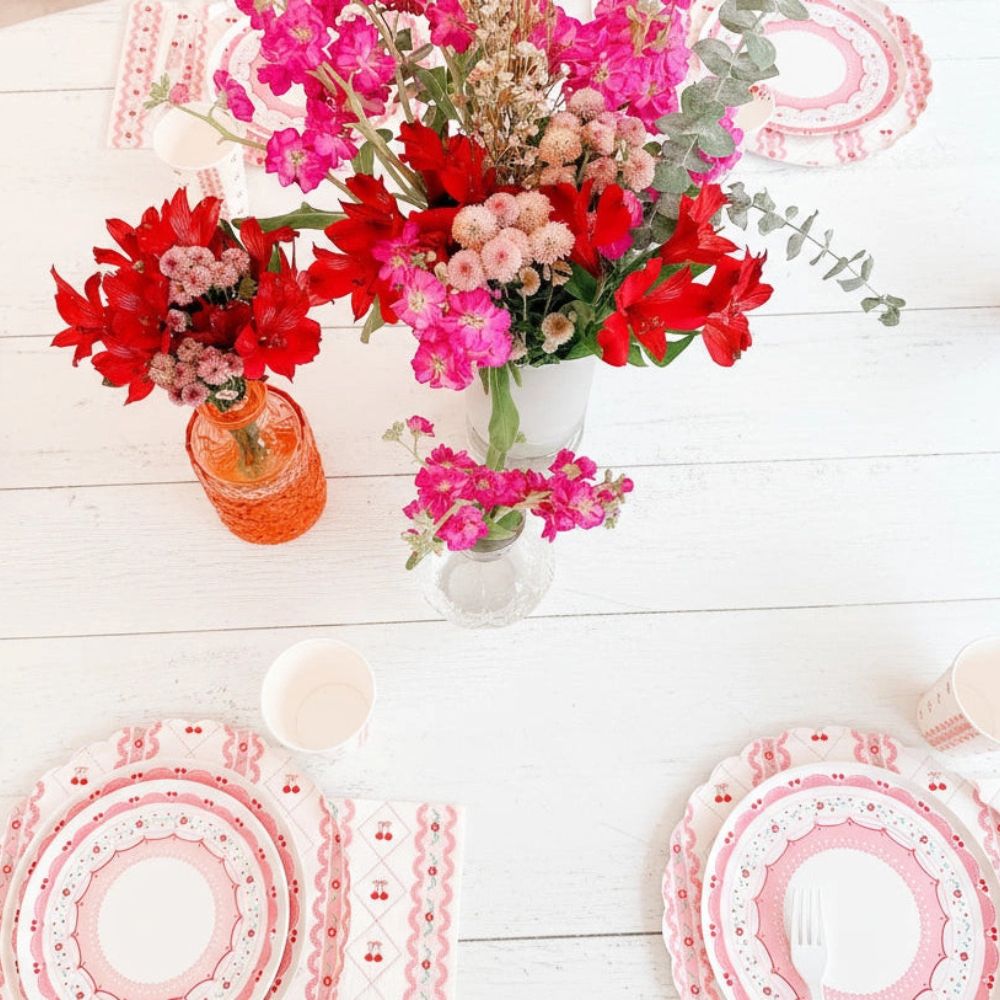 High-angle view of a complete cherry themed table setting with bright pink flowers