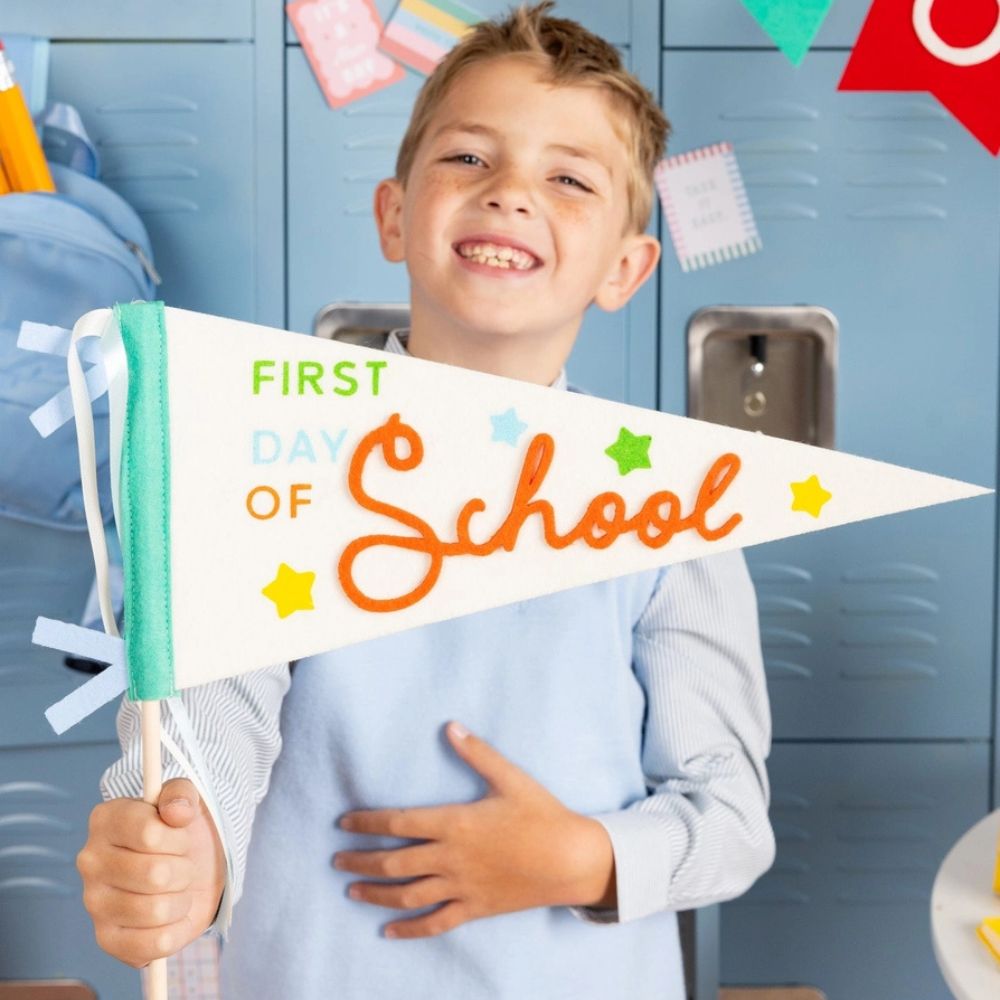 Child holding first day of school pennant smiling.