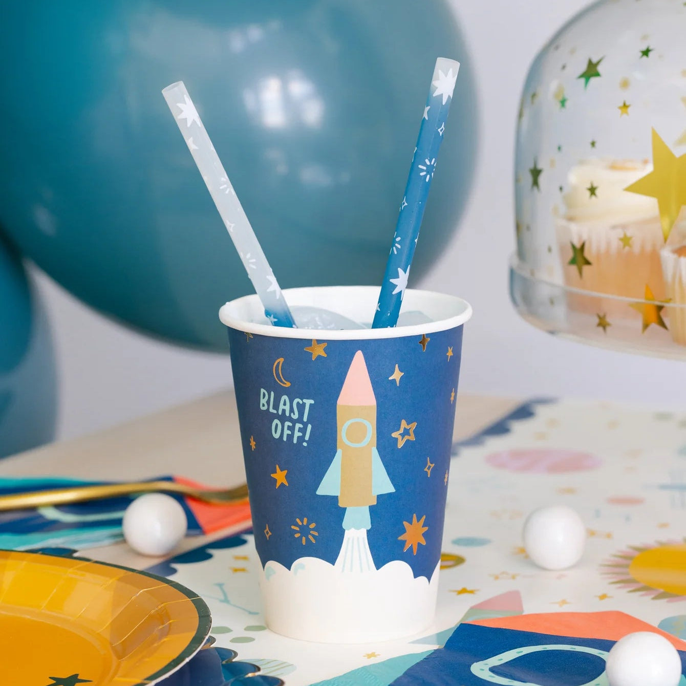 Party cup with rocket design and straw on a table with space-themed decorations