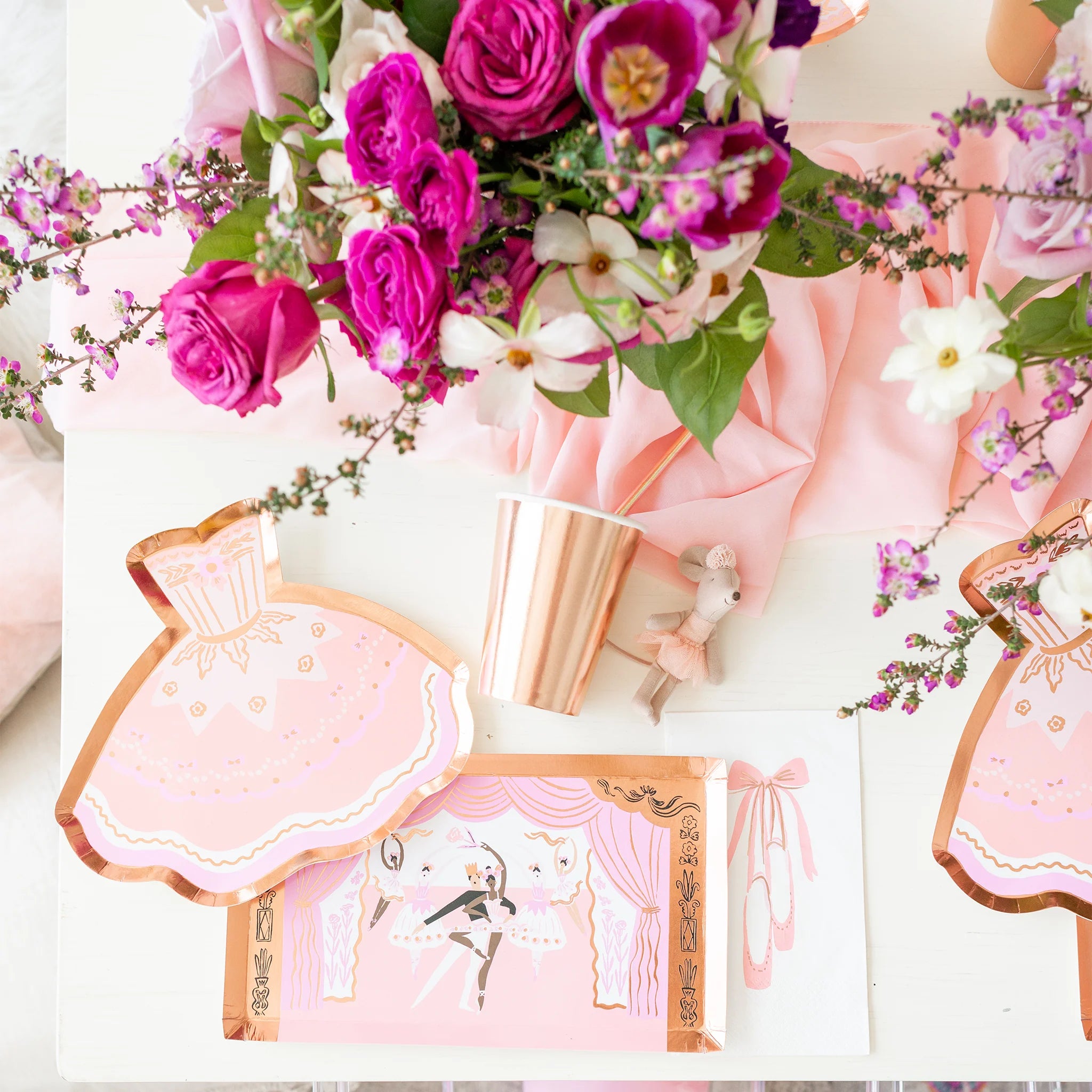 Flat-lay of a ballet-themed party table with tutu-shaped plates, floral arrangements, and rose gold cups.