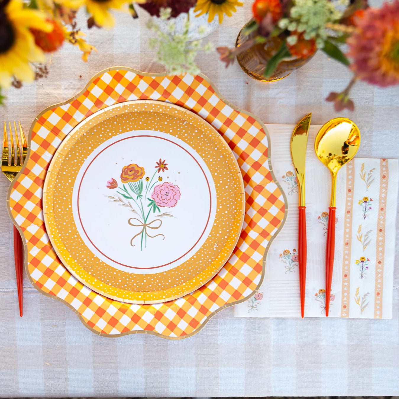 Close-up place setting showing orange gingham charger under a floral dessert plate with matching guest towel.