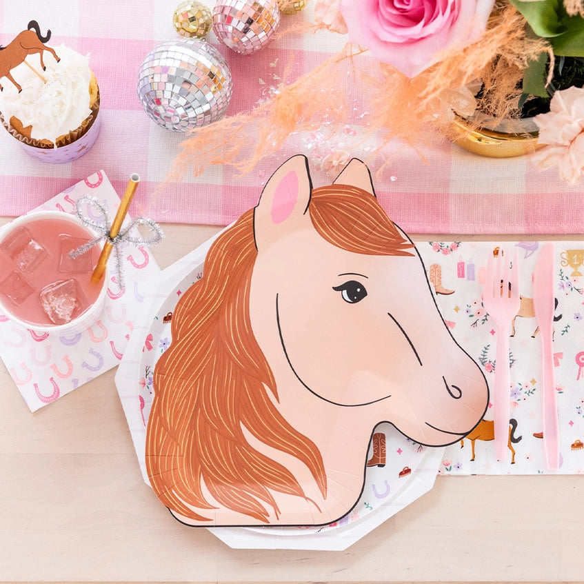 Close‑up of caramel pony silhouette plate beside horseshoe napkin, pink drink, and sparkly disco ornaments.