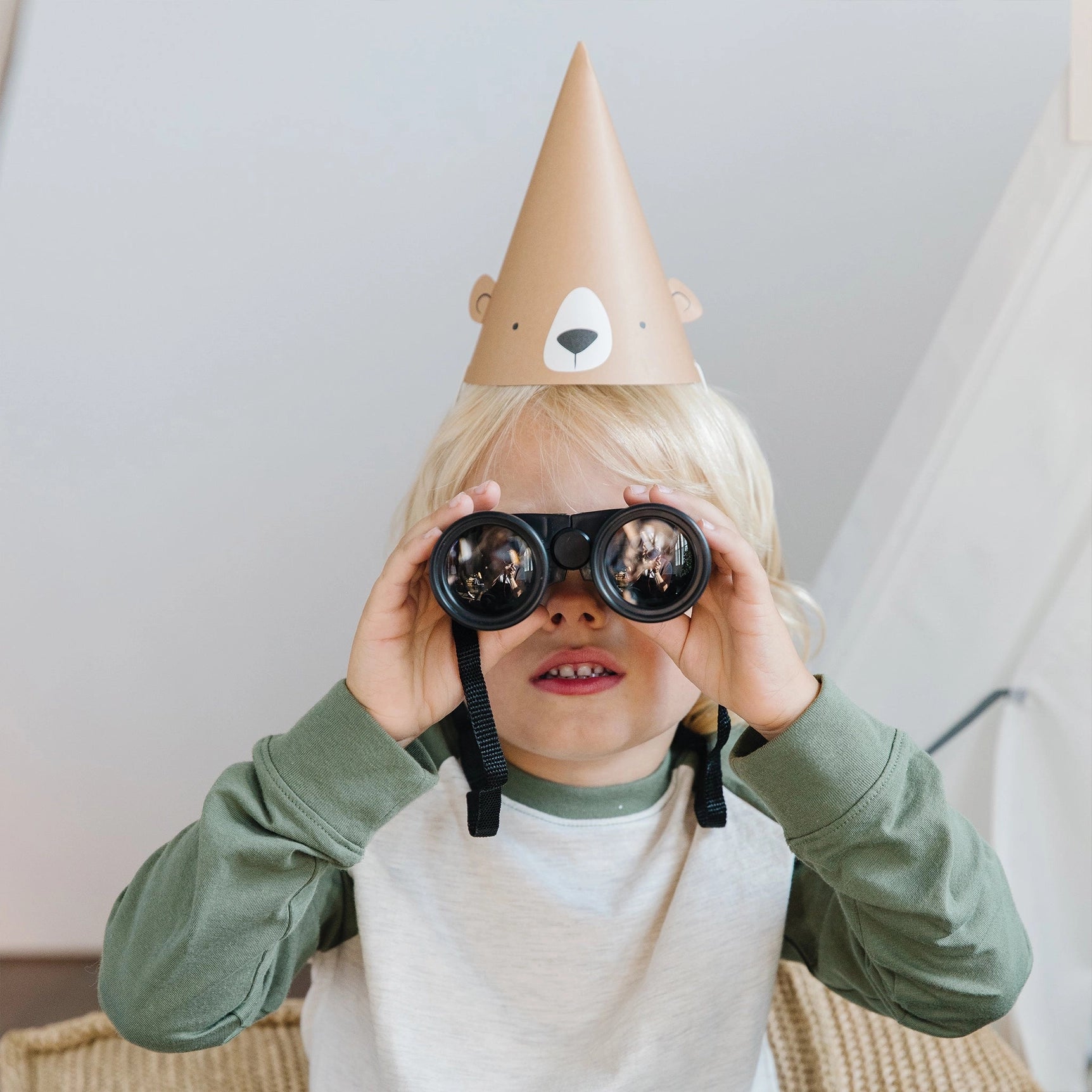 Child wearing a bear party hat and holding binoculars—perfect for a wilderness-themed birthday adventure.