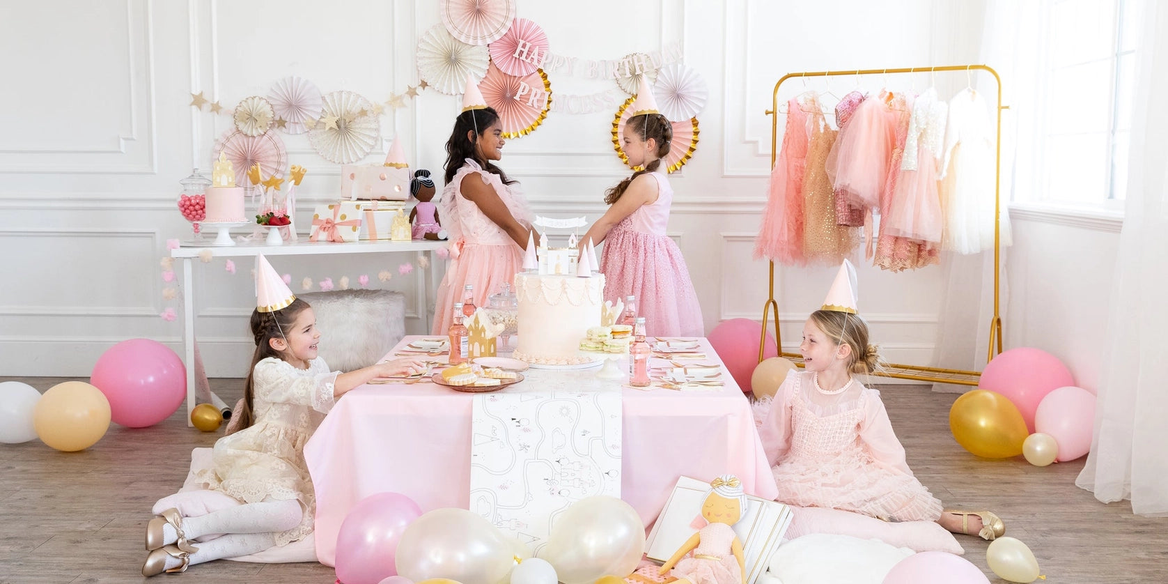 Full party scene: kids in pink dresses around dessert table, banner visible above castle cake at a princess birthday party.