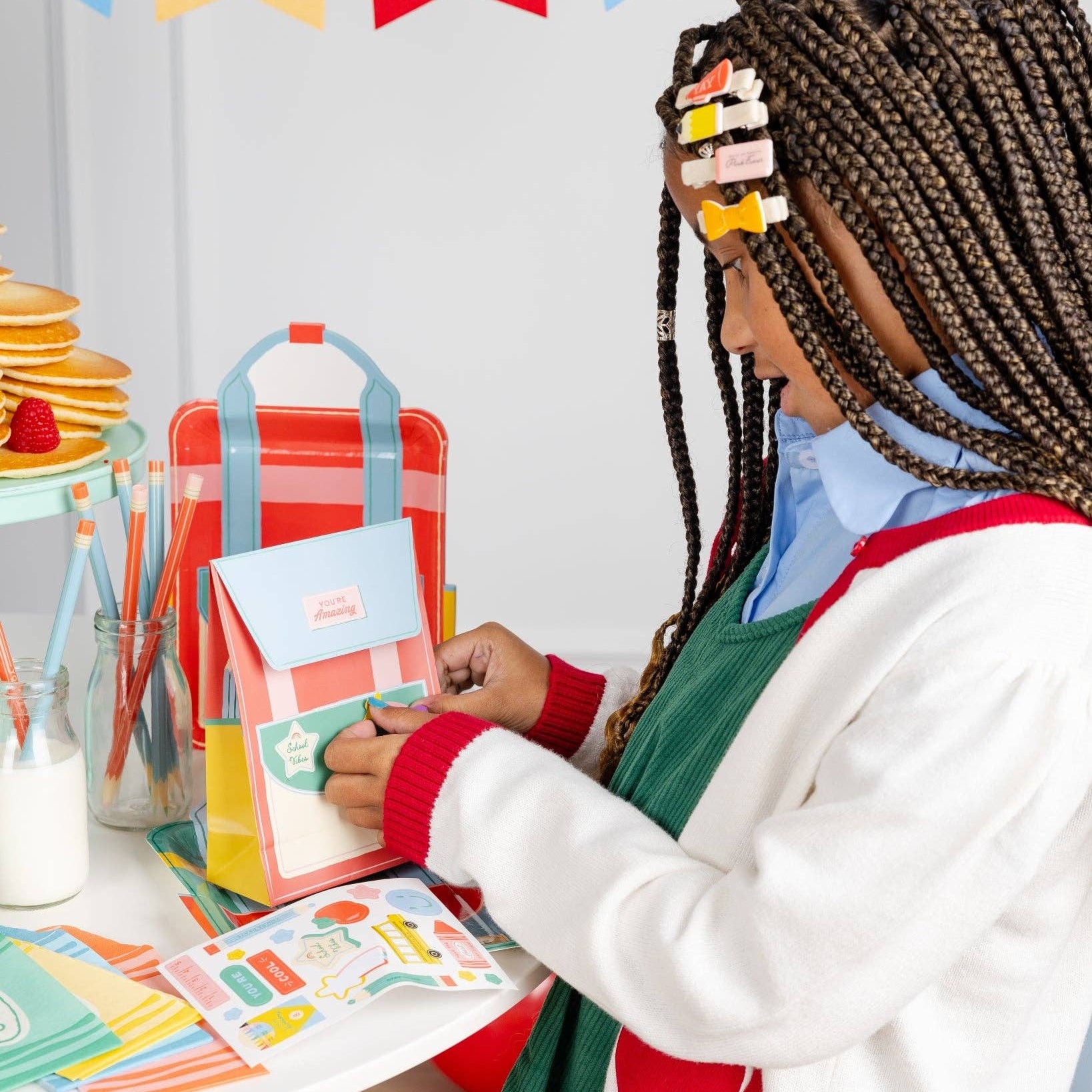Child decorating backpack treat bag with included stickers at party table.