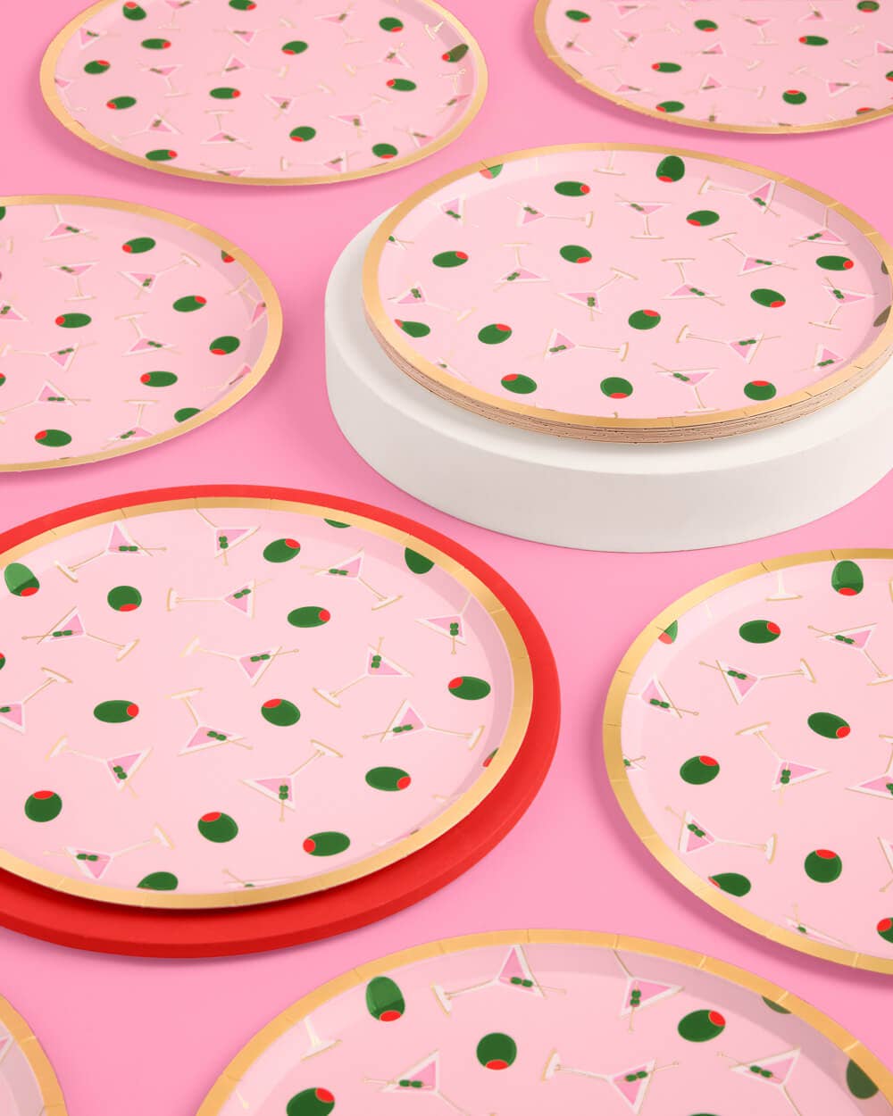 Single pink martini print paper plate close-up on pink background showing scattered martini glass and green olive print with gold foil rim