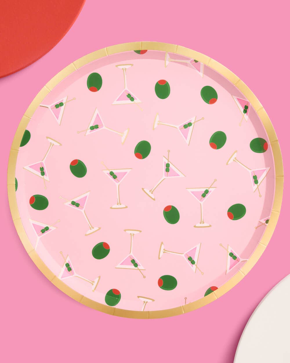 Multiple pink martini print paper plates arranged on pink background with red and white plates showing gold foil rim detail and martini olive pattern