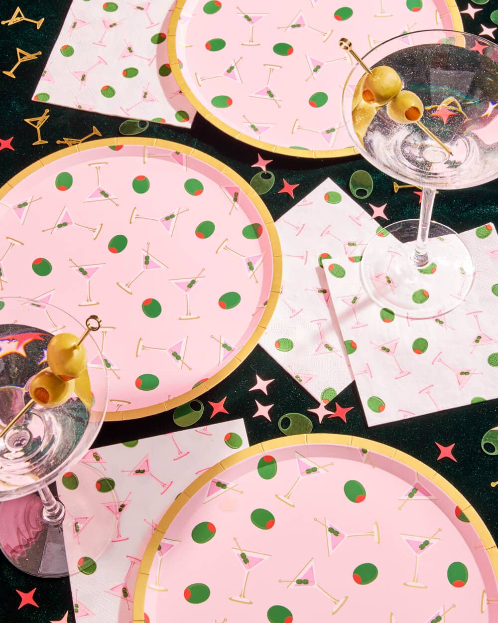 Overhead view of pink martini print paper plates with slices of pink cake on pink background showing martini glass and olive pattern with gold foil rim