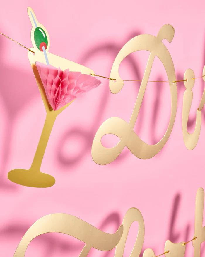 Close-up of a pop-up pink honeycomb martini glass accent piece from the Dirty Thirty gold foil birthday banner, with gold cursive letters in the background