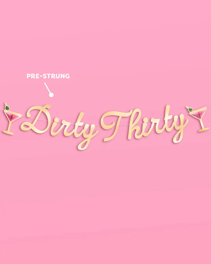 Full Dirty Thirty gold foil banner displayed flat on a pink background, with a callout label noting it is pre-strung on a gold cord
