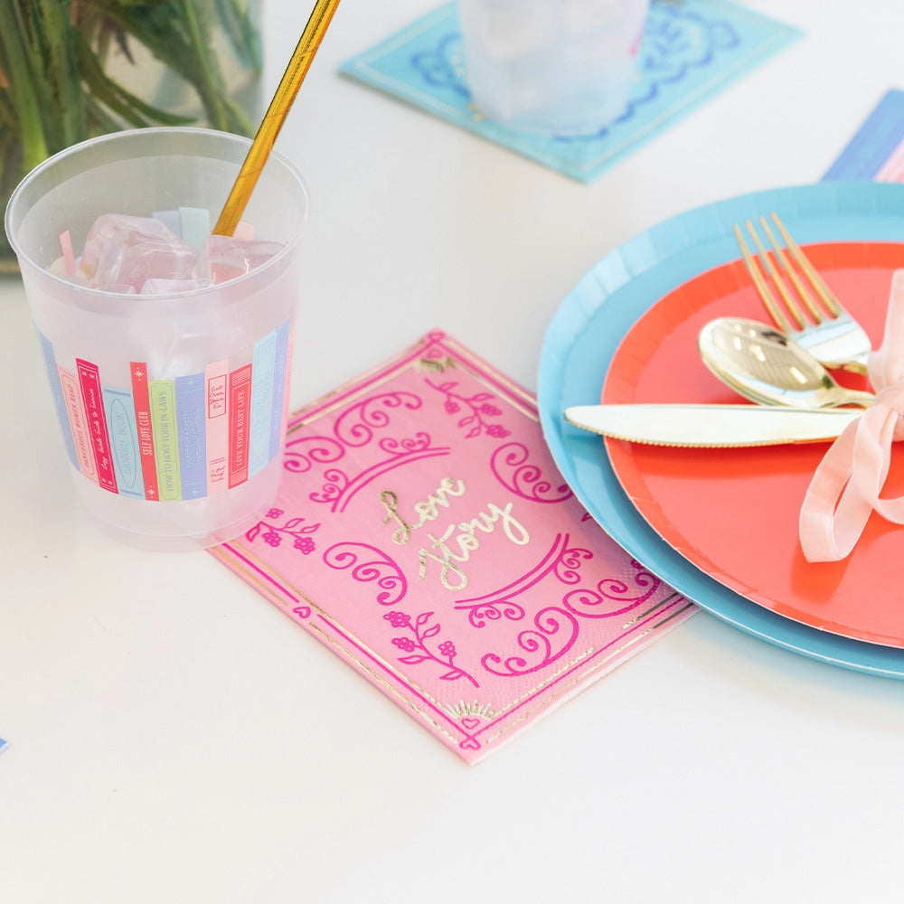 Pink 'Love Story' cocktail napkin styled with pastel-colored dinnerware and gold utensils.