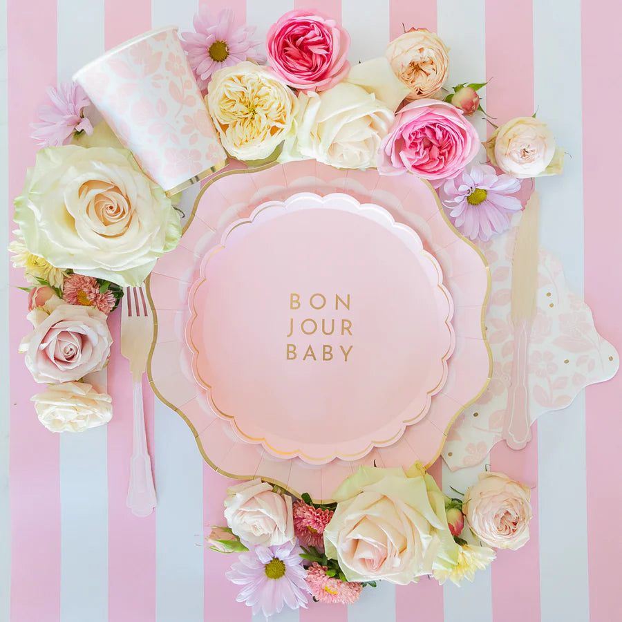 Overhead view of pink floral guest napkin layered with “Bonjour Baby” plates, cup and roses on striped runner.