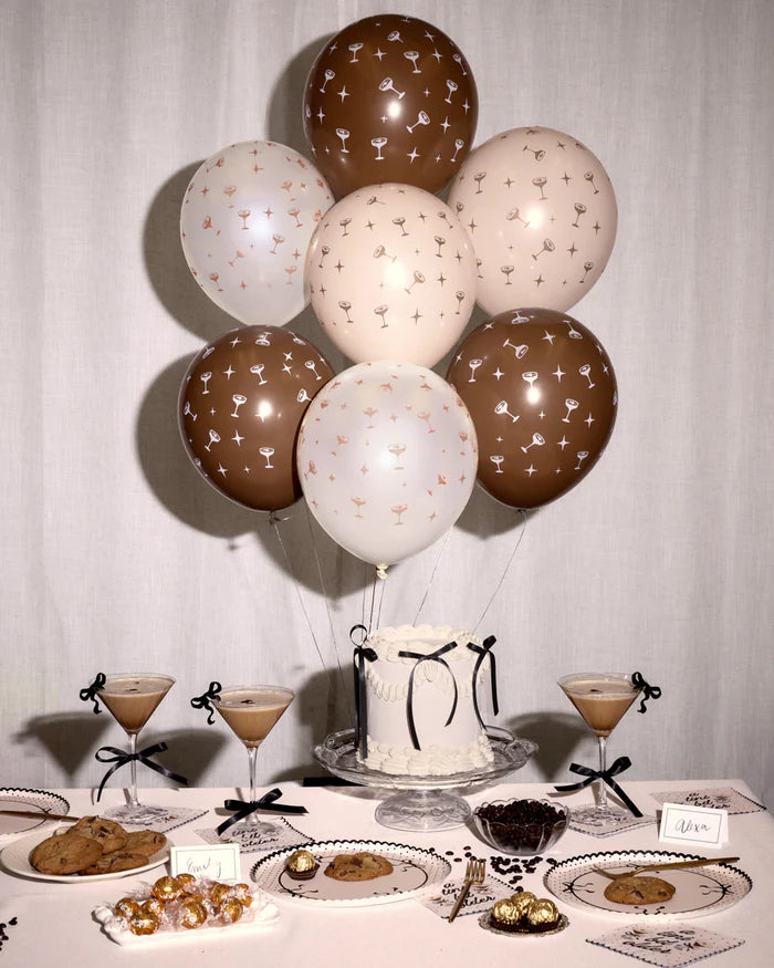 Bouquet of espresso martini print latex balloons in brown, cream, and blush floating above a styled party table with espresso martini cocktails, a white cake, and cookies