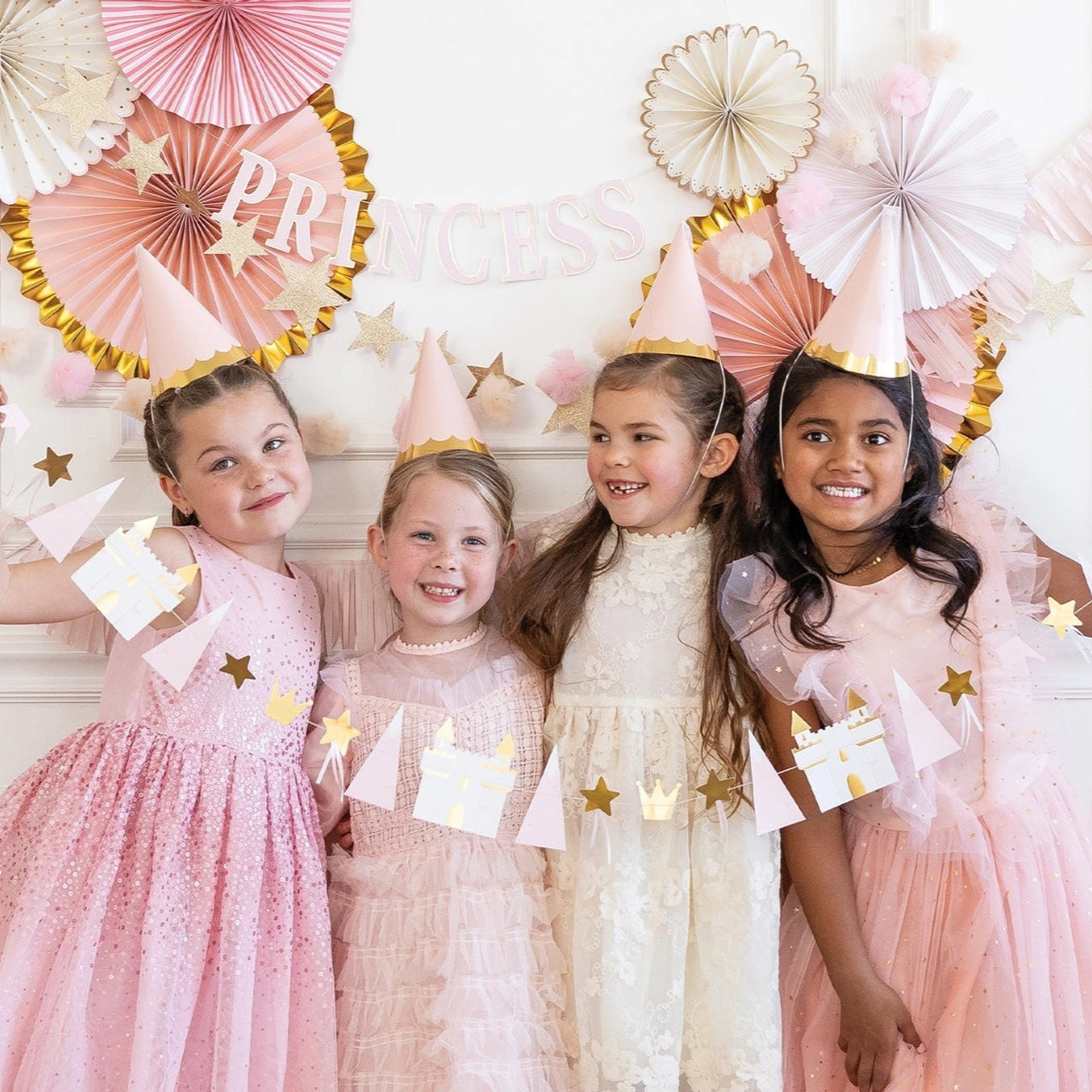 Four girls in pink party dresses wearing cone hats and holding the princess icon banner.