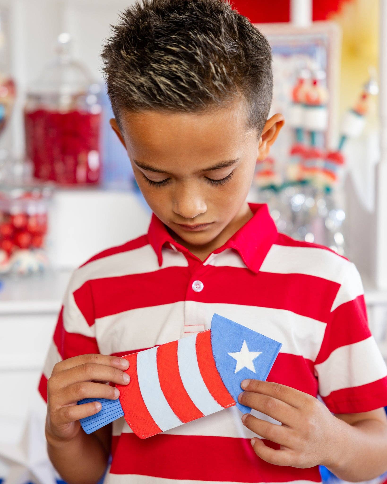 Boy in red and white striped polo holding a firecracker shaped paper napkin at a patriotic candy cart party