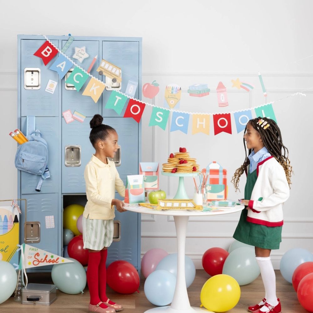 Kids celebrating first day of school with banner and decorations.