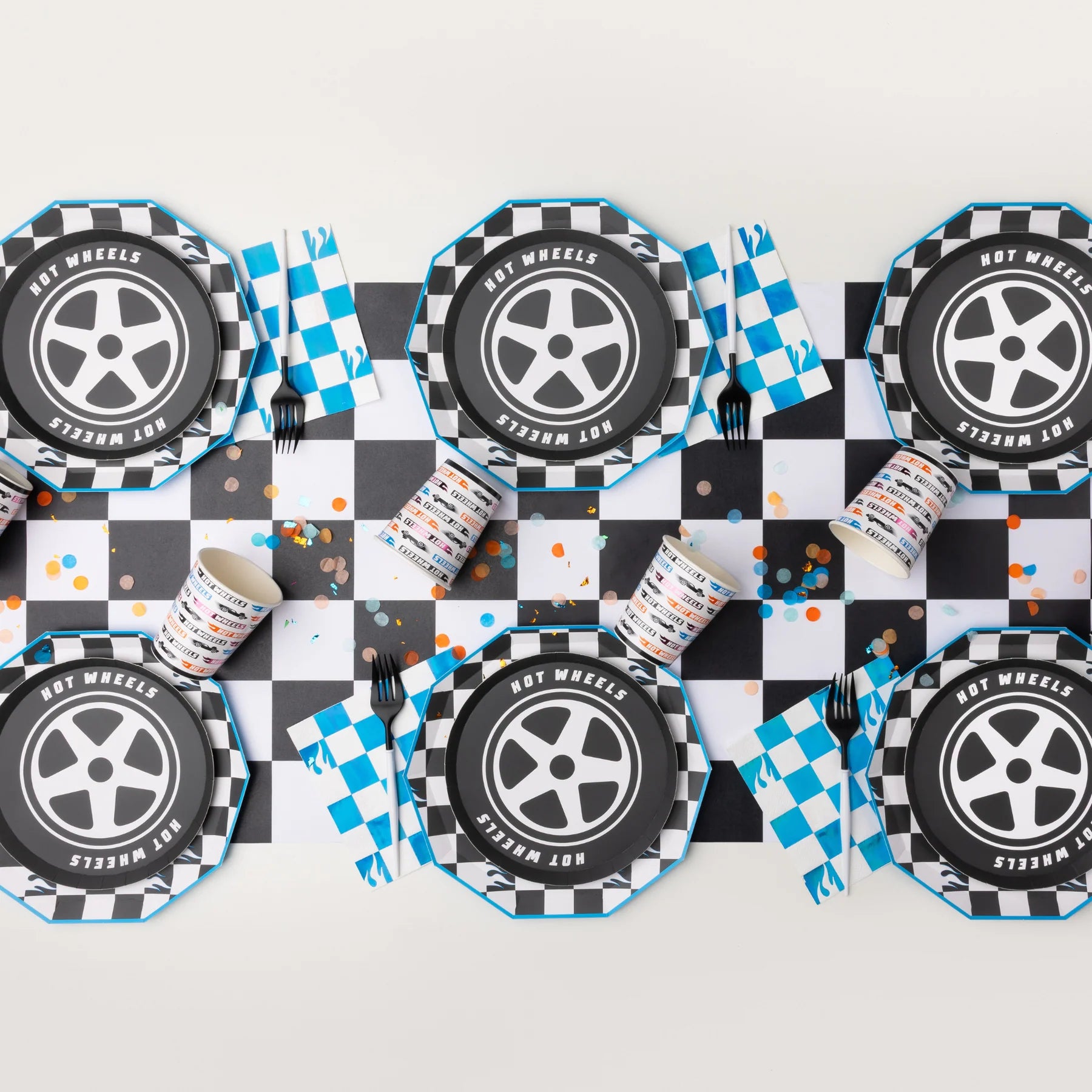 Overhead flat lay showing a table setup featuring the hot wheels party supplies plates, cups, and napkins on a checkered runner.