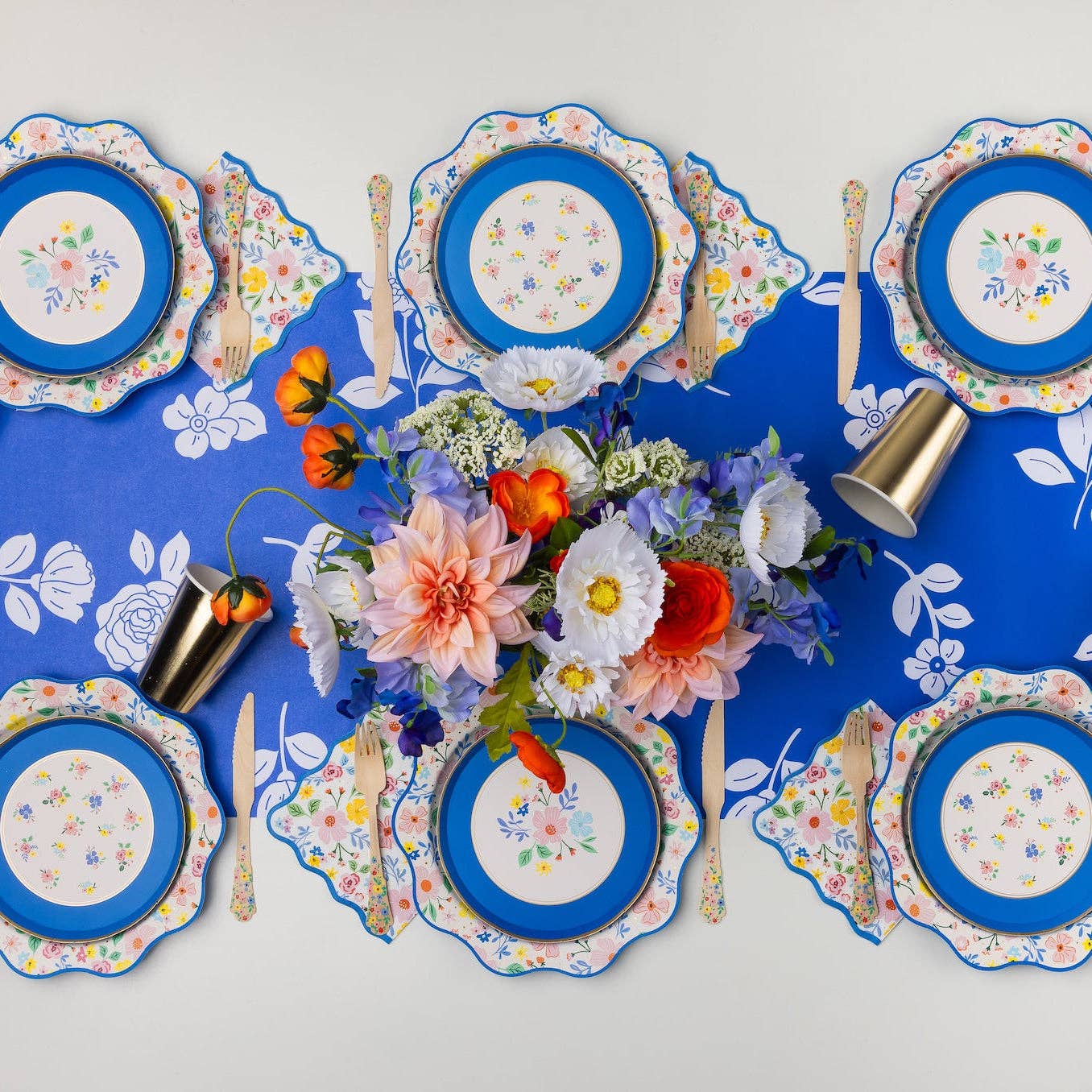 Floral party table setting with matching floral plates and blue accents.
