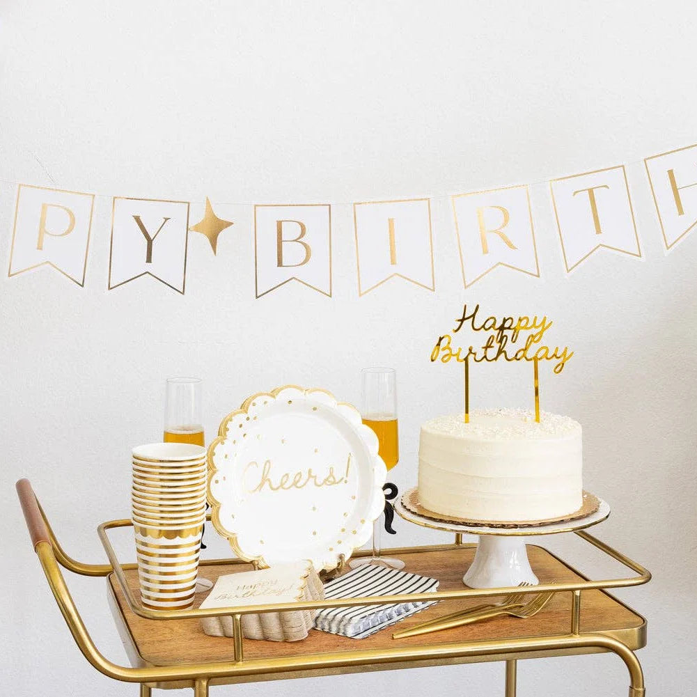 Gold birthday party bar cart with cream gold Cheers scalloped plate, gold striped cups, white cake with gold Happy Birthday topper and gold banner