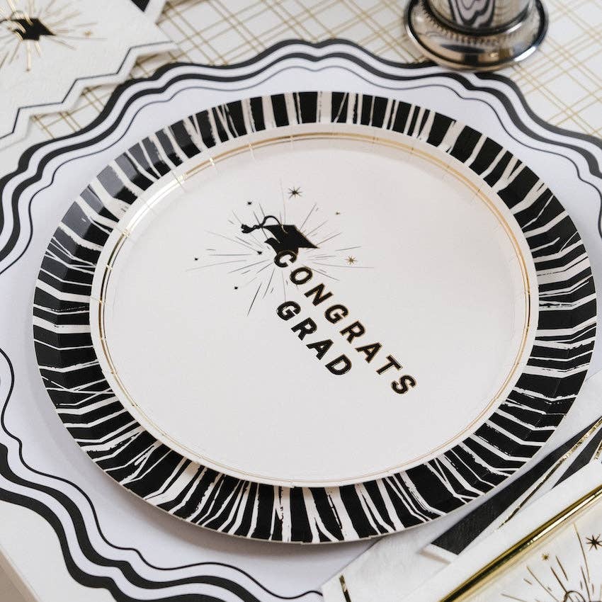 A close up of a Congrats Grad dessert plate with a gold foil striped rim for a Cap and Champagne celebration.