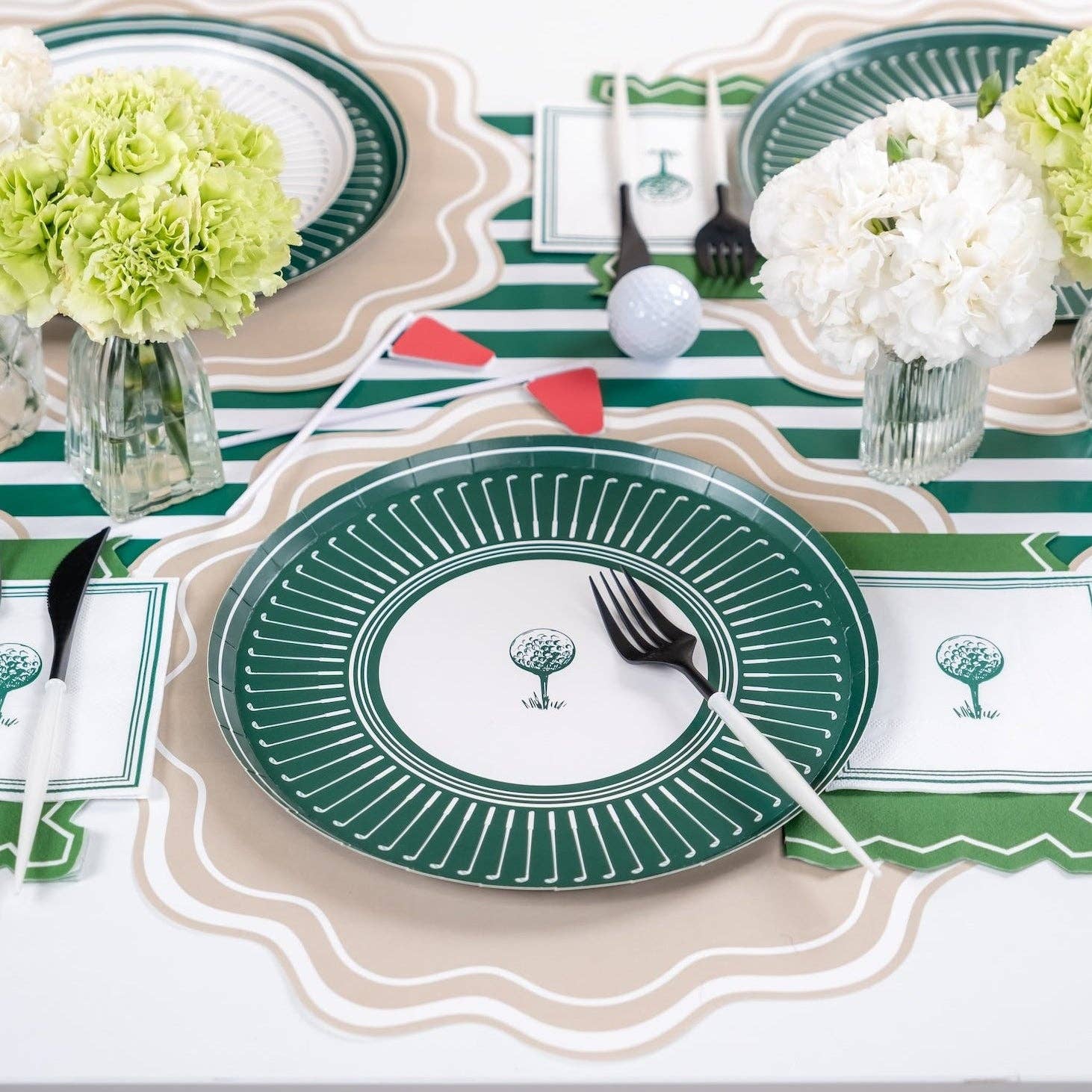 A curated golf party place setting featuring the clubhouse green plate, matching golf ball napkins, black-and-white modern cutlery, and fresh green carnations.