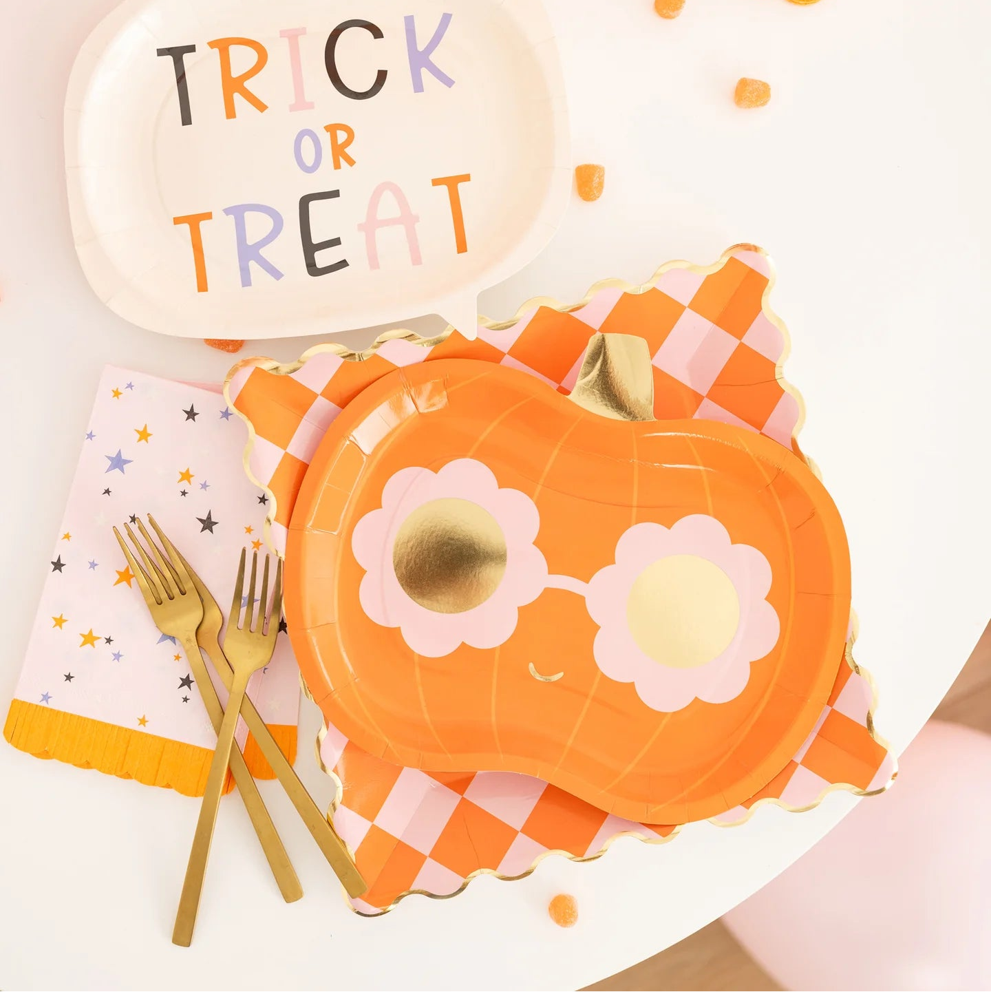 Close-up tablescape featuring groovy pumpkin plate atop orange gingham charger with pastel star napkin and gold cutlery.