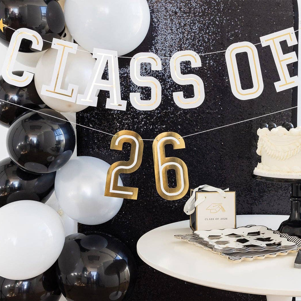 A Class of 2026 Sign hanging as a graduation photo backdrop next to white balloons and a black sequin wall.