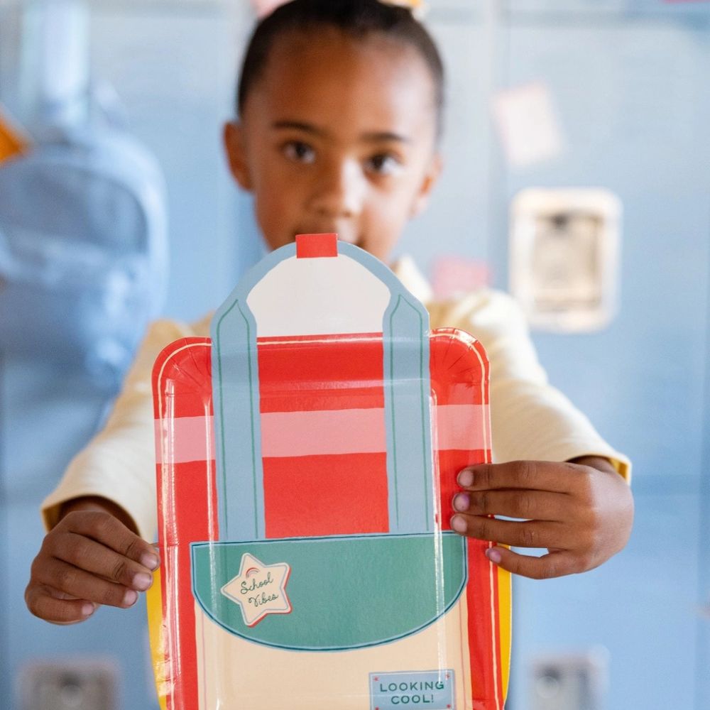 Child holding backpack shaped plate at school themed party.