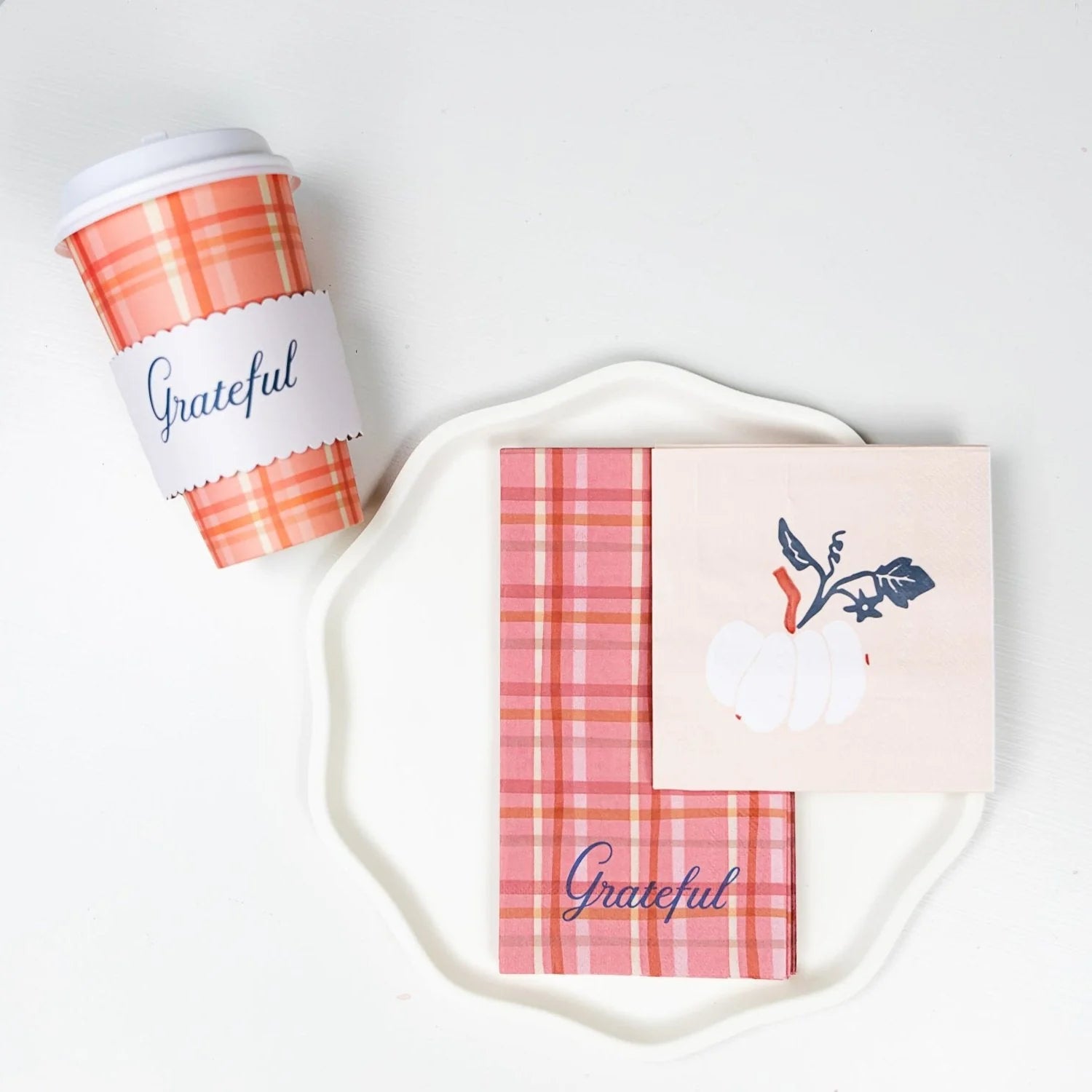 Plaid cup beside a scalloped plate with plaid guest towel and white-pumpkin napkin.