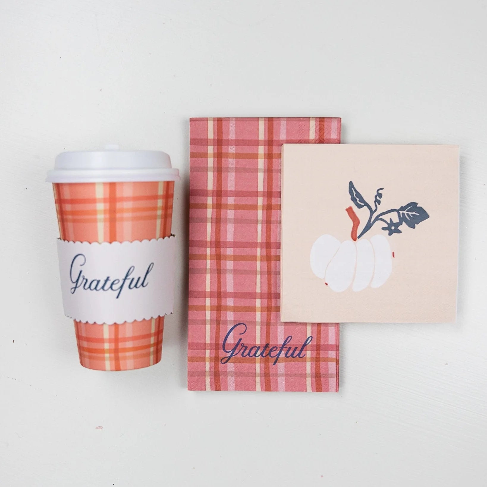 Overhead of plaid cup with “Grateful” wrap next to matching guest towel and napkin.