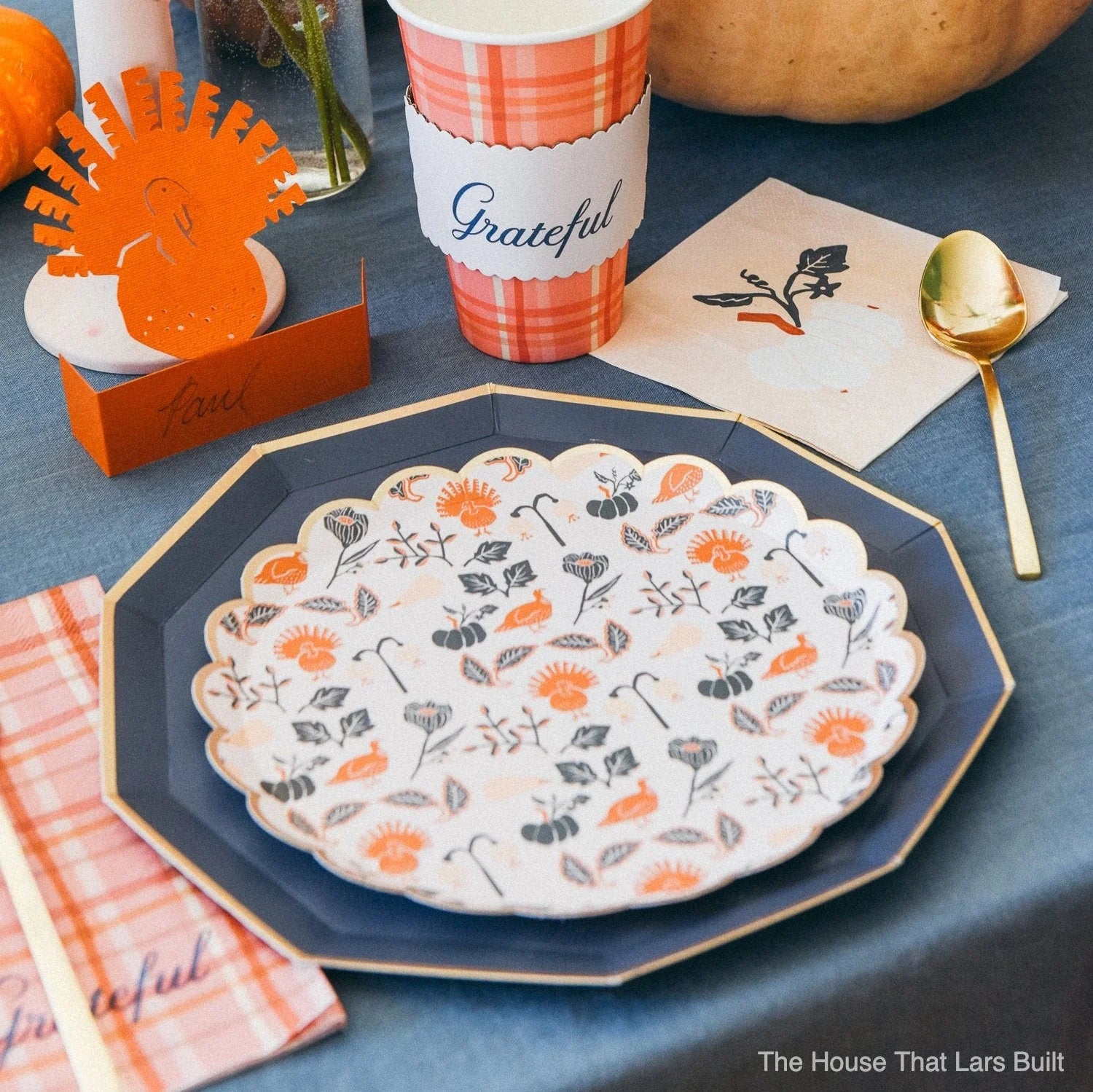 Close-up place setting showing plaid cup, pumpkin napkin, and layered plates.