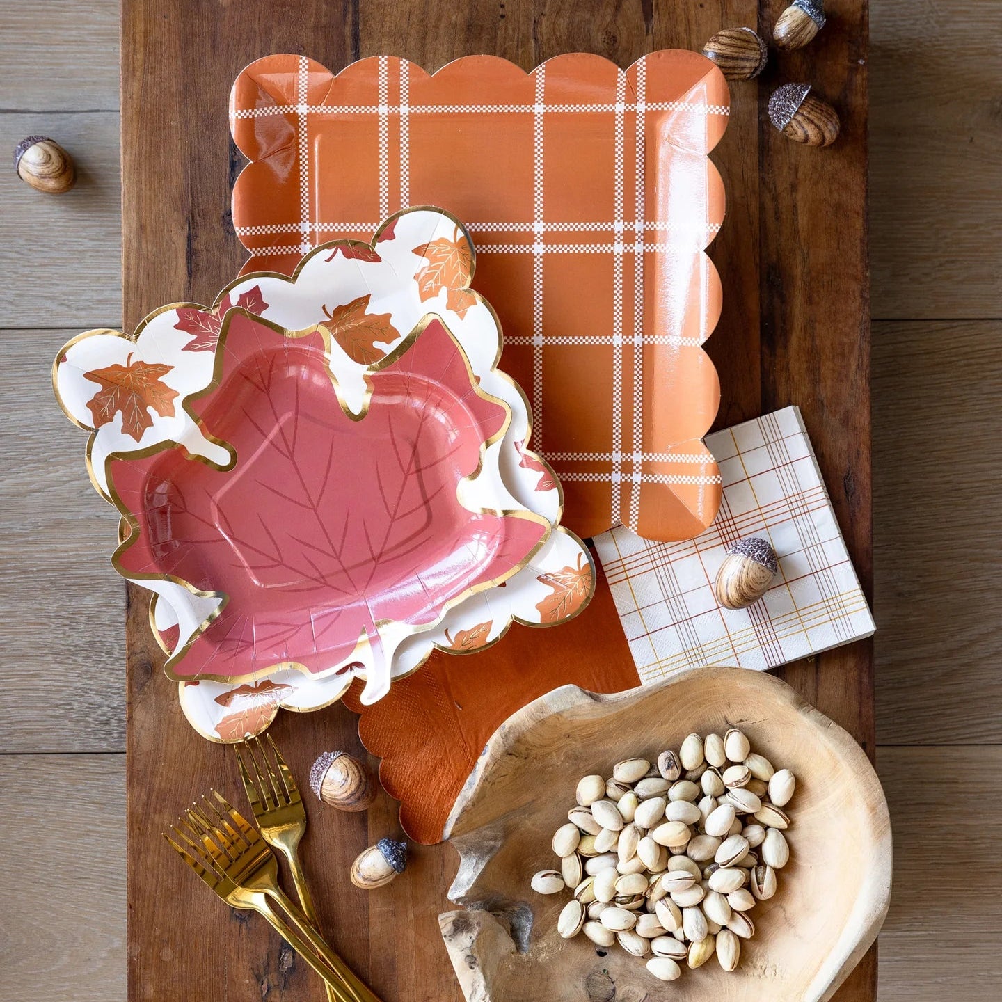 Leaf plates styled on a fall tablescape with an orange plaid tray, acorns, and nuts.
