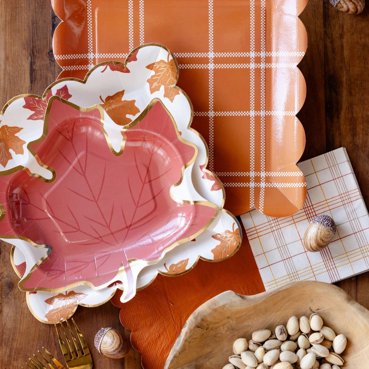 Close-up flat lay of leaf plates layered over an orange plaid tray with acorns.